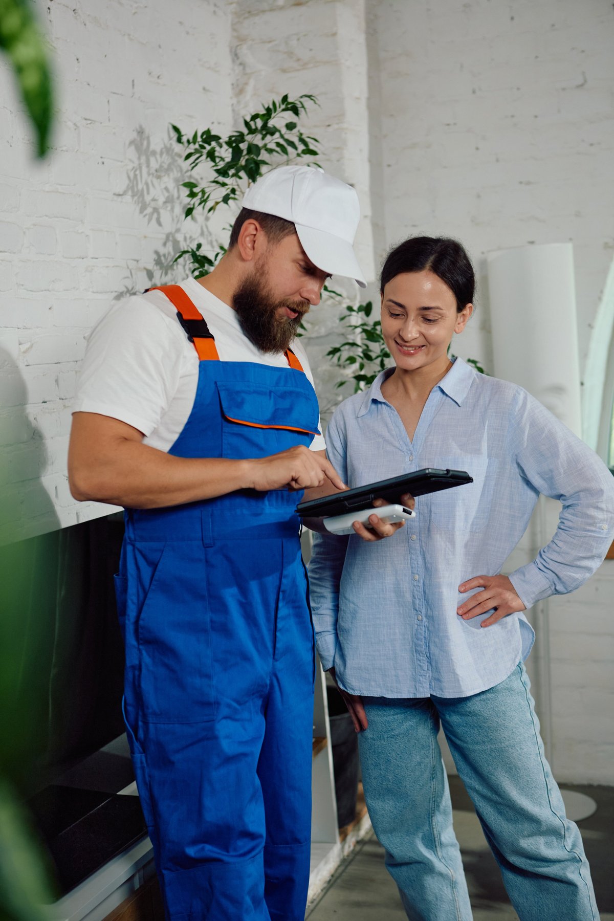 HVAC technician in a company uniform shirt demonstrating repair details to a homeowner on a tablet during an in-home service visit